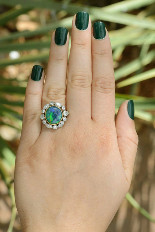 Hand wearing an ornate ring with a green gemstone against a natural background